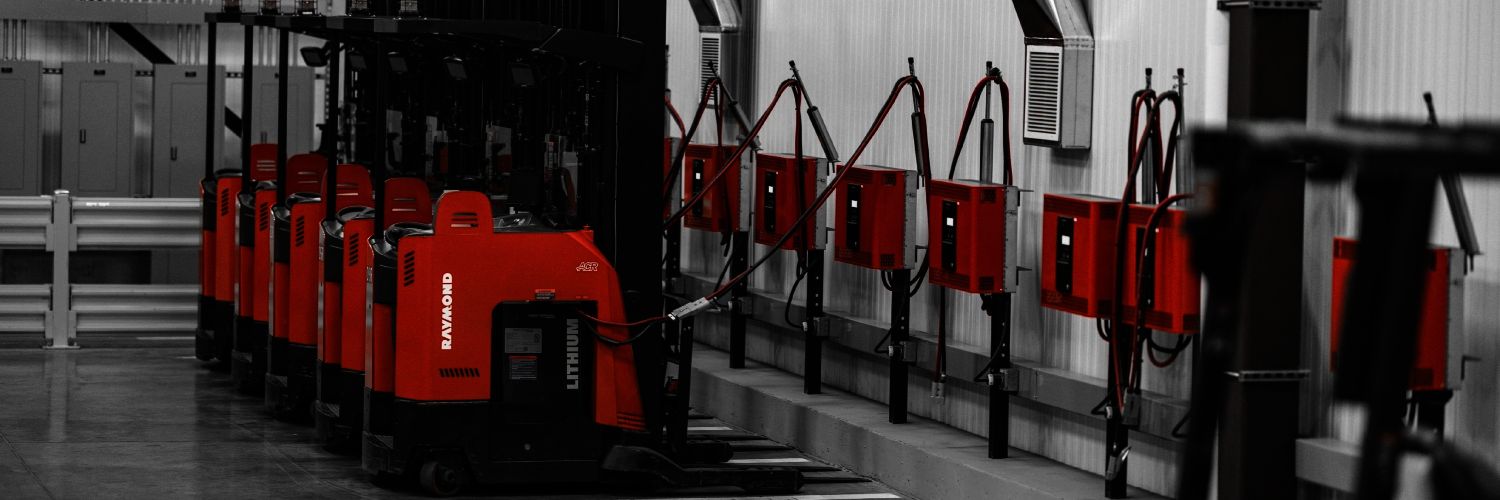 Red Raymond forklifts line up next to a battery wall charging
