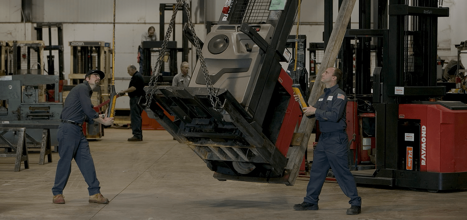 Two men lowering a red Raymond forklift for repair