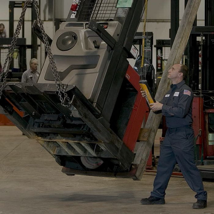 A man lowering a red Raymond forklift for repair