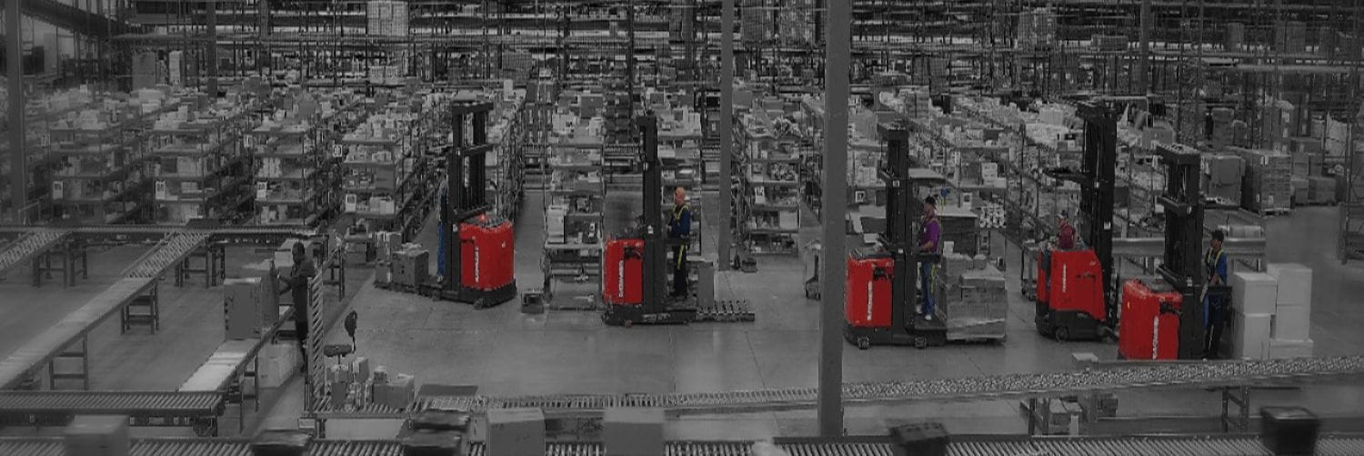 Black and white image of warehouse with red Raymond forklifts being operated