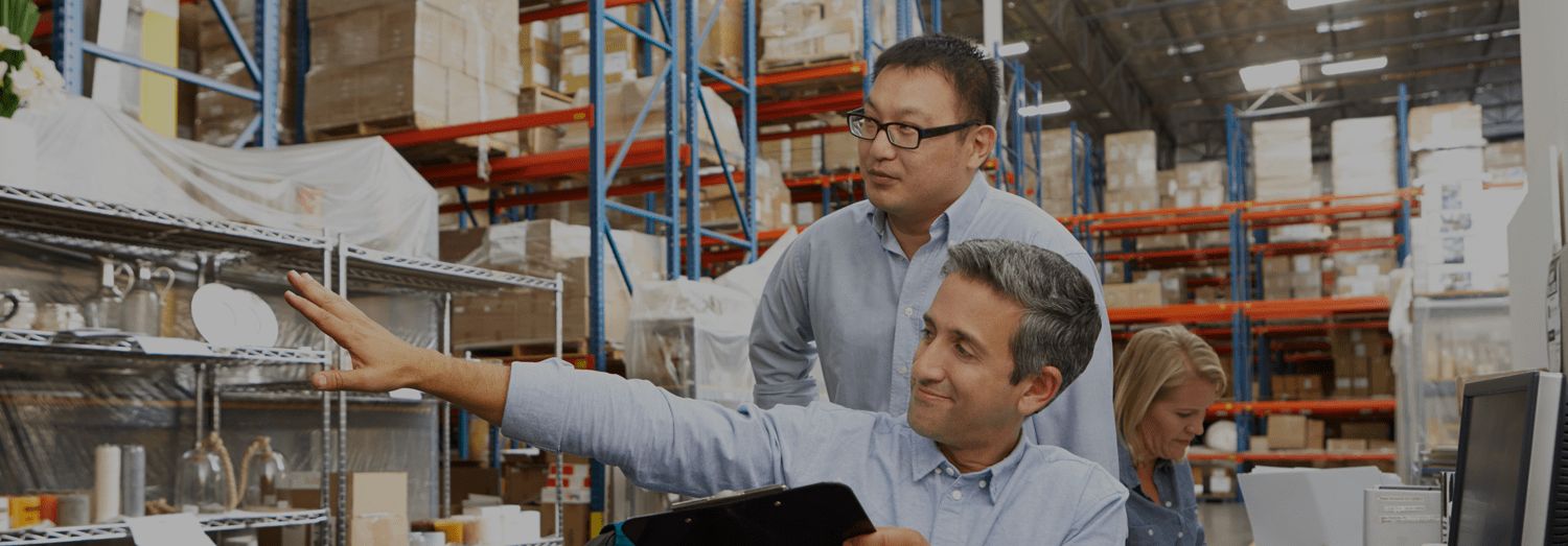 Two men in blue shirts pointing to racking. Concept for warehouse inventory management.