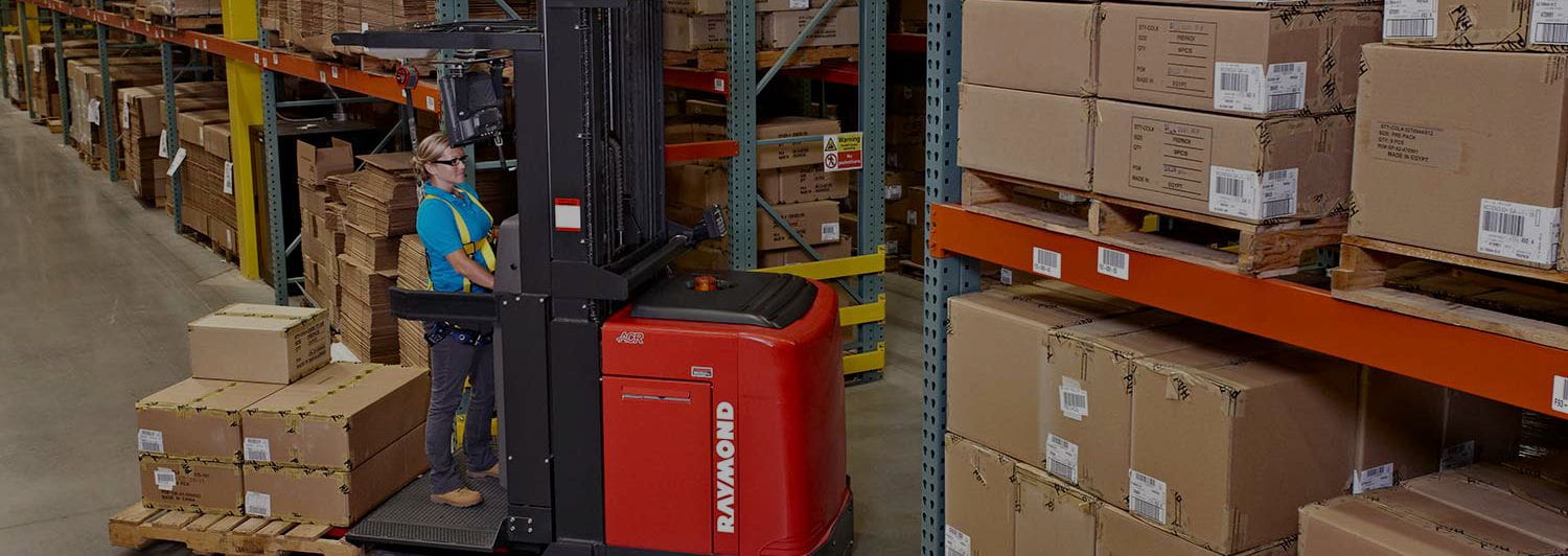 Woman in blue shirt operating a red Raymond order picker forklift in a warehouse