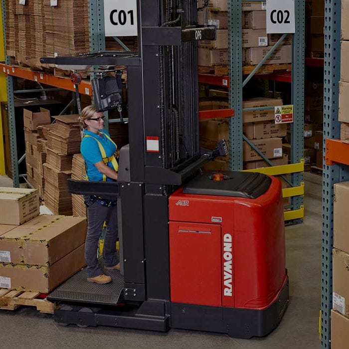 Woman in blue shirt operating a red Raymond order picker forklift in a warehouse