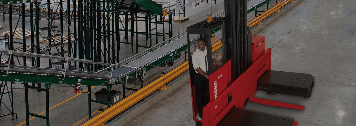 Man operating a red and black Raymond side loading forklift